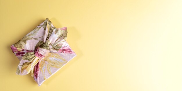 Une boîte-cadeau à la mode enveloppée dans un tissu floral dans la technique japonaise du furoshiki sur fond jaune