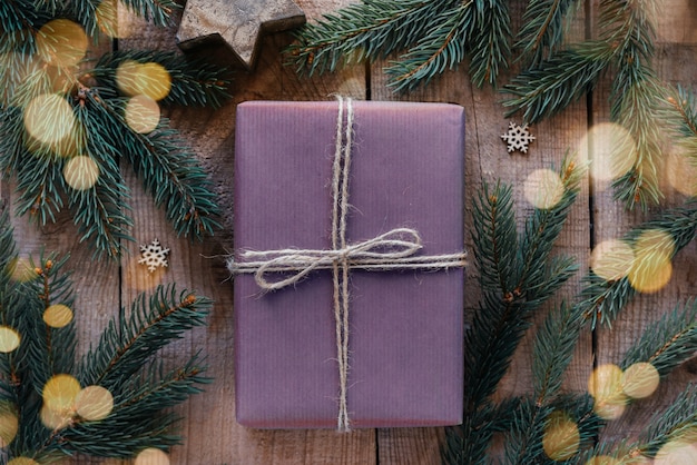 Boîte cadeau de Noël enveloppée dans du papier kraft violet et décorée d'une branche de pin sur fond de fête du nouvel an