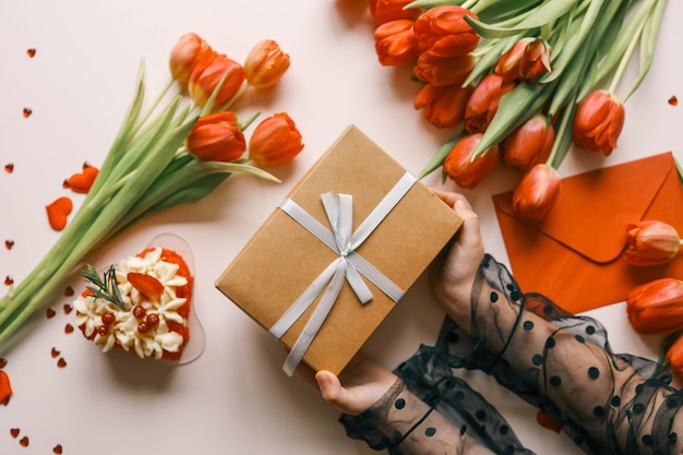 Photo boîte cadeau avec un nœud et des tulipes dans les mains d'une fille fond festif