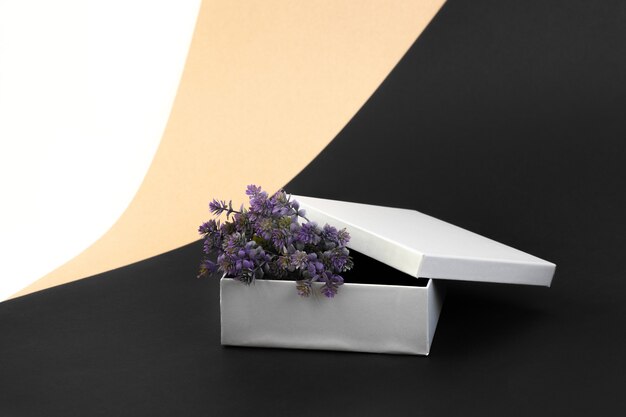 Boîte cadeau ouverte en argent avec des fleurs artificielles violettes