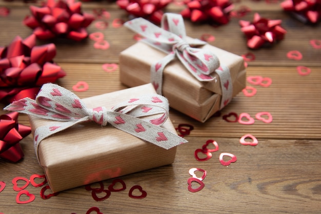 Photo boîte cadeau en papier brun kraft avec des arcs rouges et des confettis, sur une table en bois. saint valentin, anniversaire.