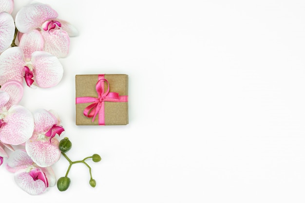 Boîte cadeau présente à plat avec ruban rose avec des fleurs d'orchidées sur la vue de dessus de fond blanc.