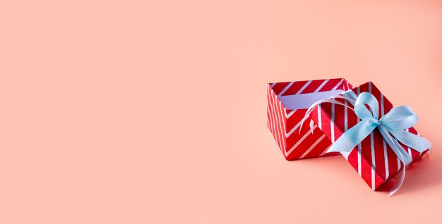 Boîte-cadeau rayé rouge de Noël sur l'espace rose. Composition minimale créative. Bannière.