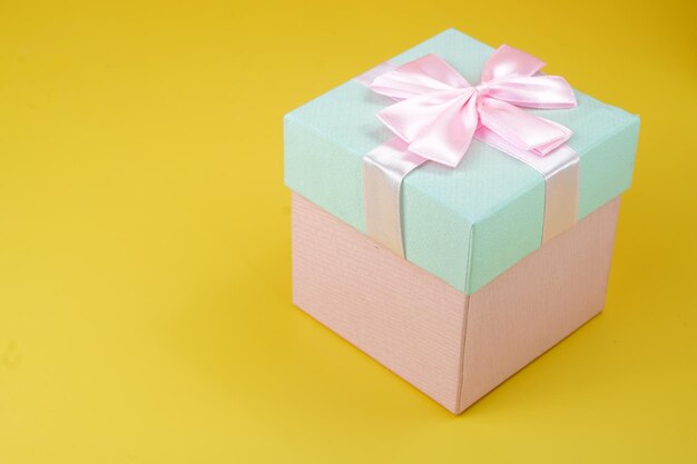 Boîte cadeau rose et cyan avec arc de ruban isolé sur fond jaune en studio