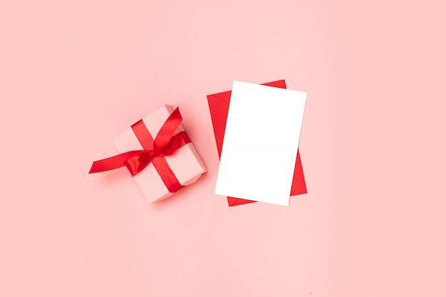 Boîte cadeau surprise enveloppée dans du papier rose avec un arc rouge, modèle d'enveloppe rouge vierge sur fond rose