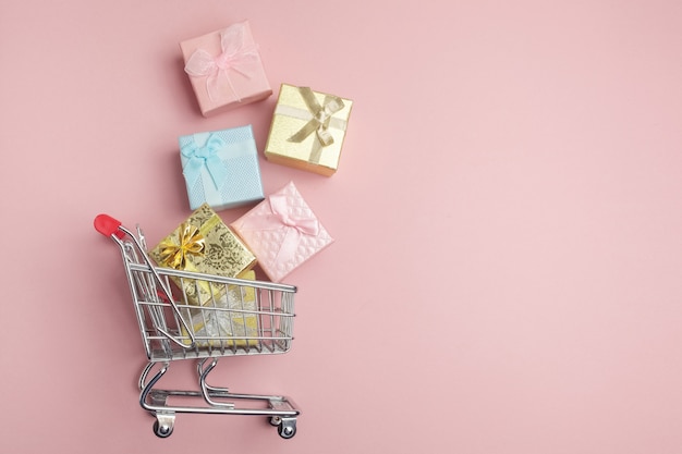 Boîte de cadeaux colorés, panier de supermarché sur fond rose