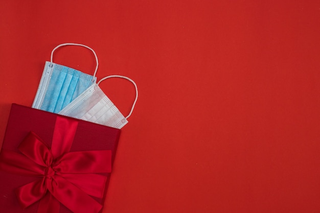 Boîte avec cadeaux et masques médicaux sur fond rouge. concept de se protéger et d'isoler le jour de Noël et la Saint-Valentin.