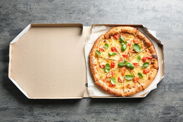 Boîte en carton avec une délicieuse pizza Margherita sur table grise