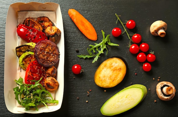 Boîte en carton avec de délicieux légumes grillés sur table sombre