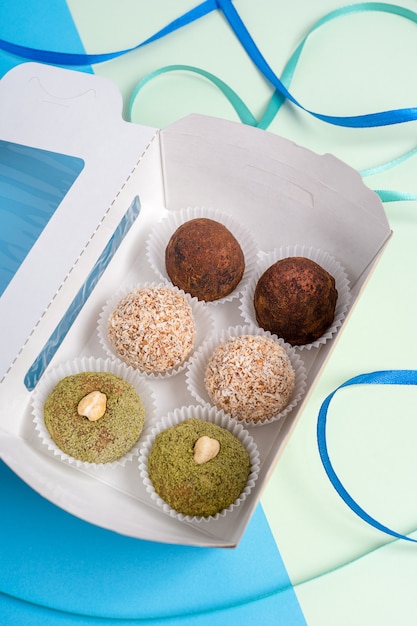 Boîte en carton ouvert avec une variété de truffes aux noix vegan portant sur fond bleu et vert coloré