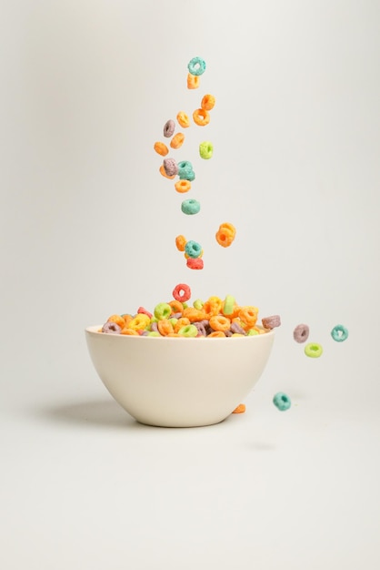 Photo boîte de céréales colorées pour le petit-déjeuner du matin. flocons de maïs tombant dans le bol blanc. mouvement. espace de copie.