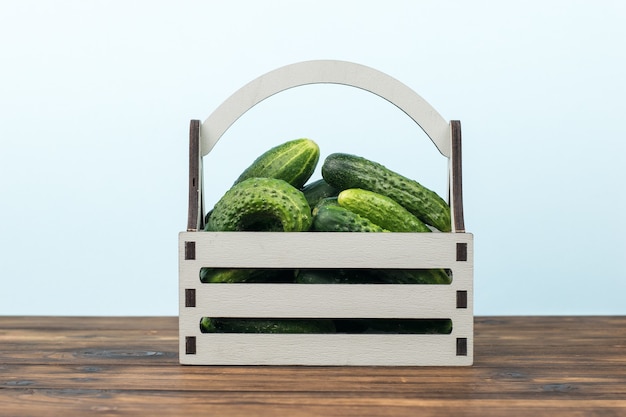 Une boîte de concombres frais sur une table en bois sur fond bleu.