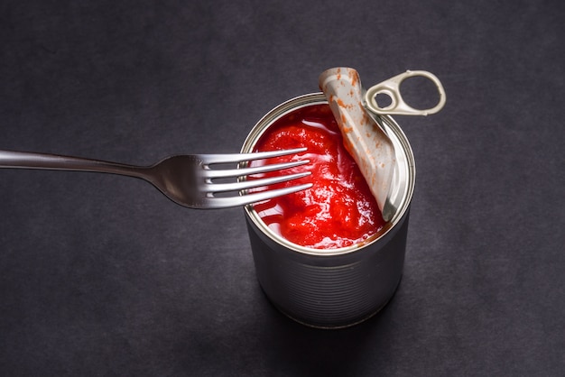 Boîte de conserve ouverte avec des tomates en conserve, sur fond noir