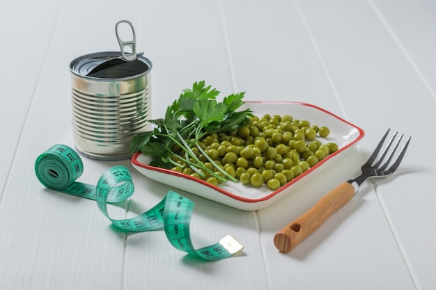 Boîte de conserve, pois verts, fourchette et ruban à mesurer sur une table en bois. Nourriture végétarienne diététique.