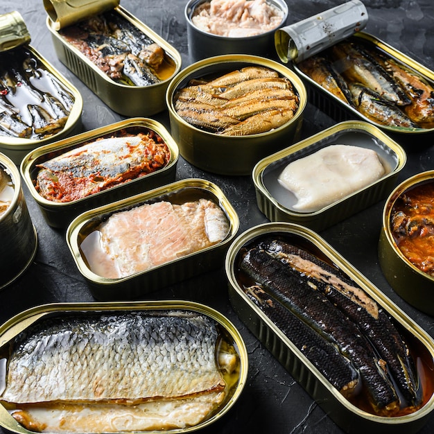 Boîte de conserve de Saury, maquereau, sprats, sardines, sardine, calmar, thon Ouvert et fermé sur fond d'ardoise noire vue de côté carré.