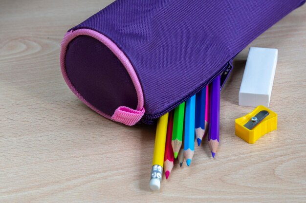 boîte à crayons violet avec des peintures colorées et d'autres fournitures scolaires sur un bureau en bois clair