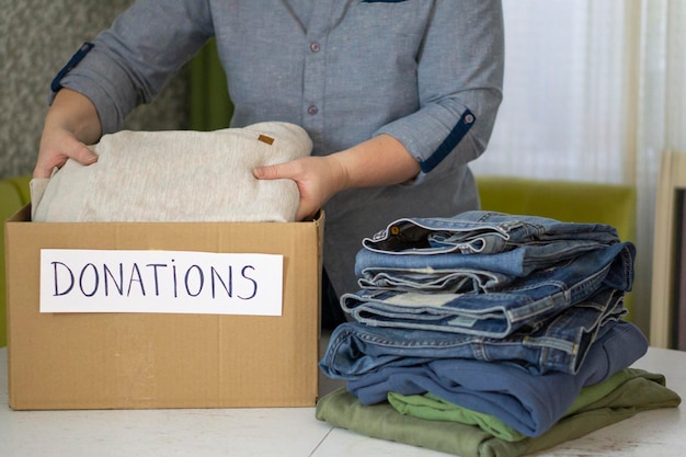 Photo la boîte de dons pour les vêtements est sur la table. les mains de la femme plient soigneusement les vêtements. concept de don et de charité