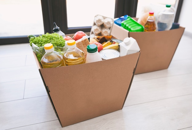 La boîte écologique en carton pleine avec des produits de l'épicerie sur le sol à la maison près de la porte