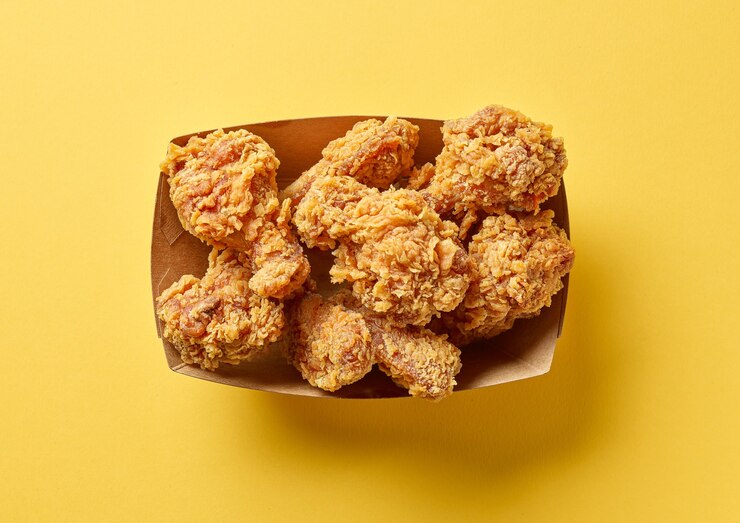 Photo boîte à emporter en papier d'ailes de poulet frites sur fond jaune, vue de dessus