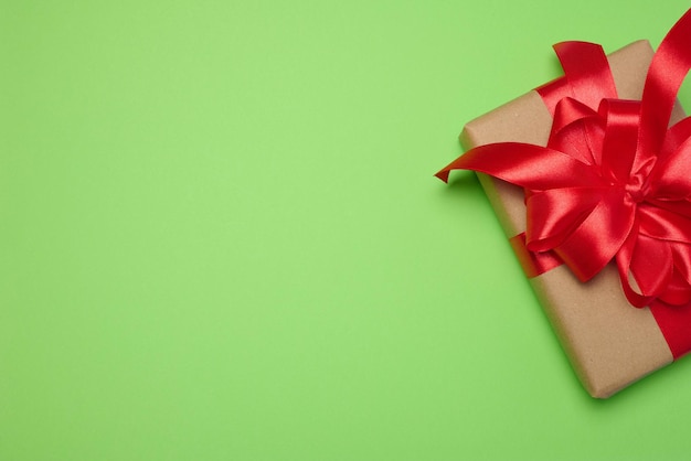 Boîte enveloppée d'un ruban rouge et d'un papier artisanal brun sur un fond vert