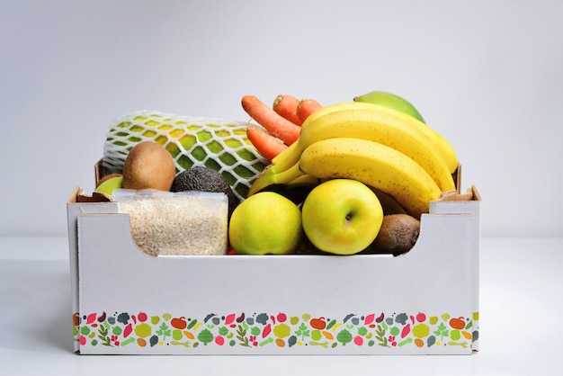 Boîte d'épicerie avec des légumes et des fruits sur fond de cuisine blanc