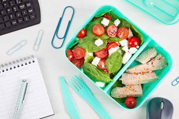 Boîte à lunch à emporter avec salade fraîche et thon sur le bureau avec des fournitures de bureau.