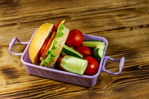 Boîte à lunch avec des hamburgers et des légumes frais sur une table en bois