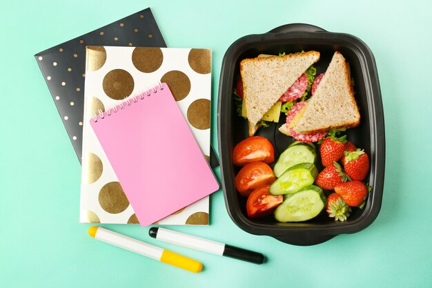 Boîte à lunch avec de la nourriture et de la papeterie sur fond turquoise