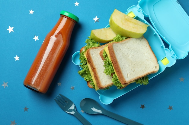 Boîte à lunch avec de la nourriture savoureuse sur fond bleu