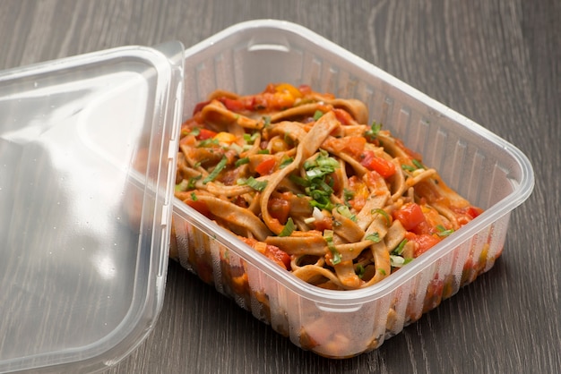 Boîte à lunch en plastique avec des spaghettis à la sauce tomate et ciboulette.