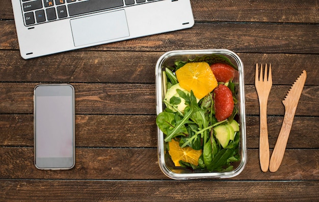 Photo boîte à lunch avec salade végétalienne saine d'orange et d'herbes de pamplemousse sur le lieu de travail