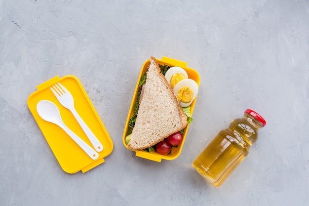 Boîte à lunch avec sandwich et différents produits sur fond gris