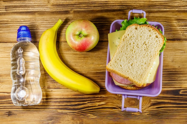 Boîte à lunch avec des sandwichs bouteille d'eau banane et pomme sur une table en bois Vue de dessus