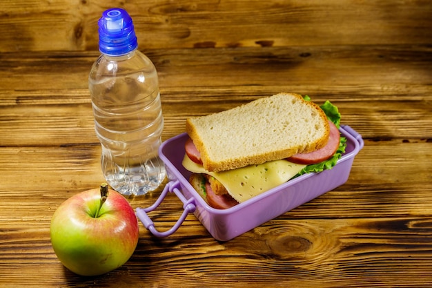 Boîte à lunch avec sandwichs bouteille d'eau et pomme sur une table en bois