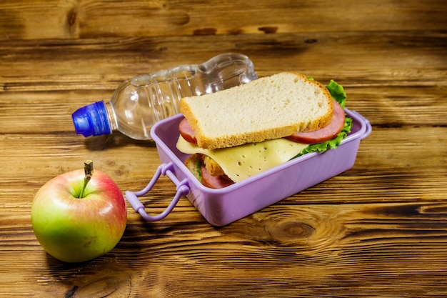 Boîte à lunch avec sandwichs bouteille d'eau et pomme sur une table en bois