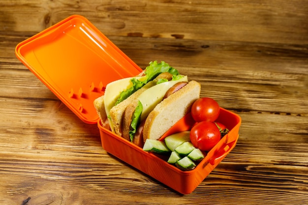 Boîte à lunch avec sandwichs et légumes frais sur une table en bois