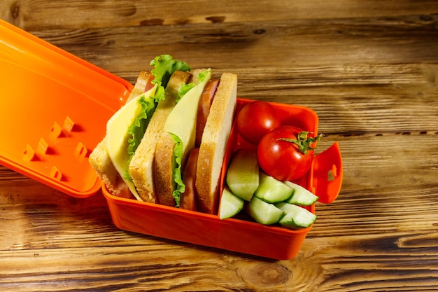 Boîte à lunch avec sandwichs et légumes frais sur une table en bois