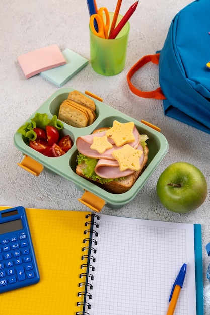 Boîte à lunch scolaire saine avec sandwich et salade sur le lieu de travail près du sac à dos Fournitures scolaires livres pomme et une bouteille d'eau