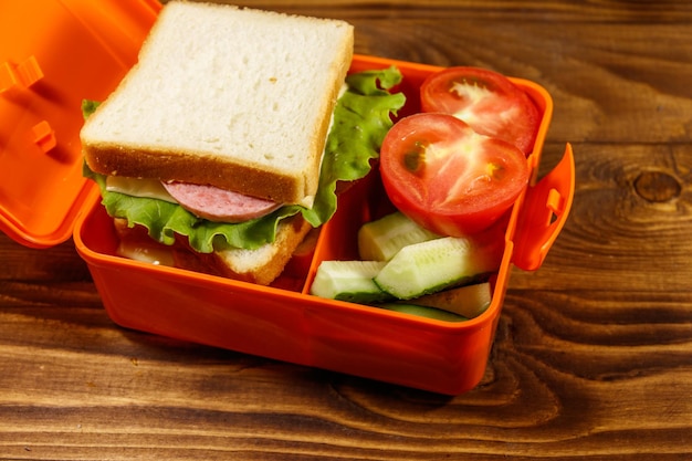 Boîte à lunch scolaire avec sandwich et légumes frais sur table en bois