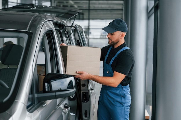 Avec boîte en mains Le livreur en uniforme est à l'intérieur avec voiture et avec commande