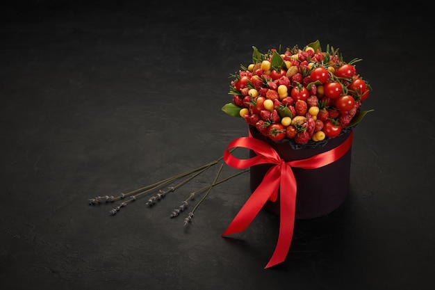 Boîte noire avec un ruban rouge rempli de tomates fromage saucisse sur fond noir