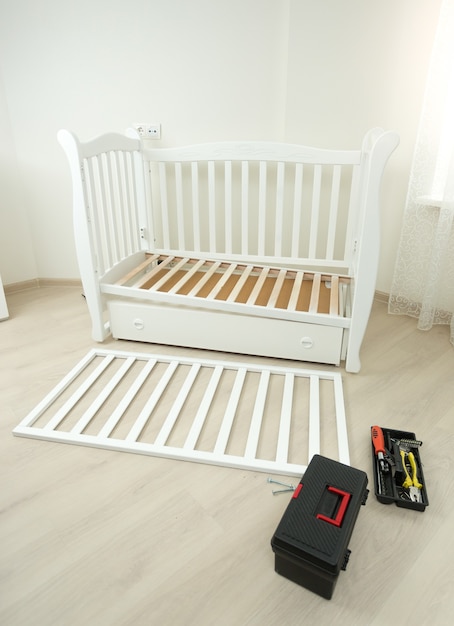 Boîte à outils allongée sur le sol à côté d'un lit bébé en bois démonté