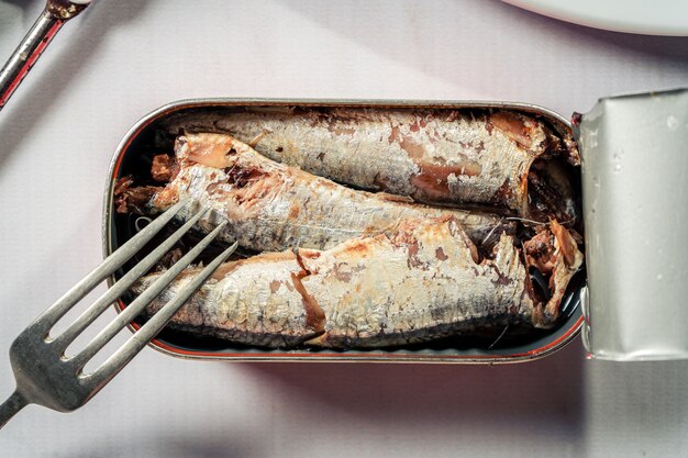 Boîte ouverte de sardines dans l'huile à côté d'une fourchette sur une surface en marbre blanc. Produit alimentaire marin