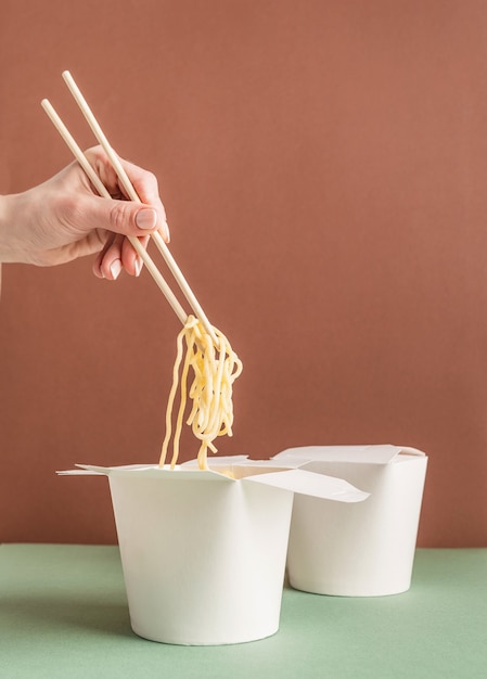 Photo boîte de papier wok ouverte pour la conception de maquettes. main de femme tenant des nouilles avec des baguettes