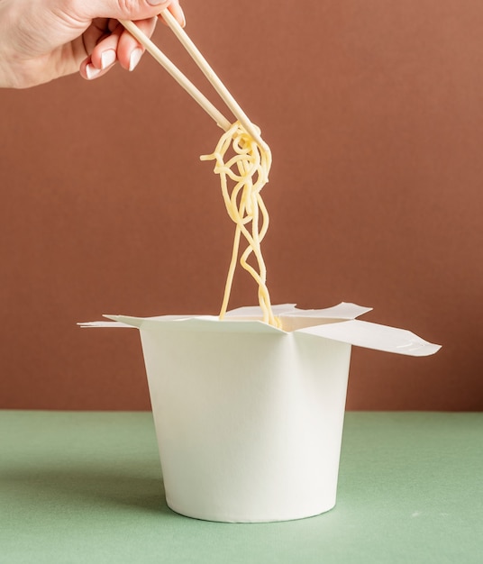 Boîte de papier WOK ouverte pour la conception de maquettes. Main de femme tenant des nouilles avec des baguettes