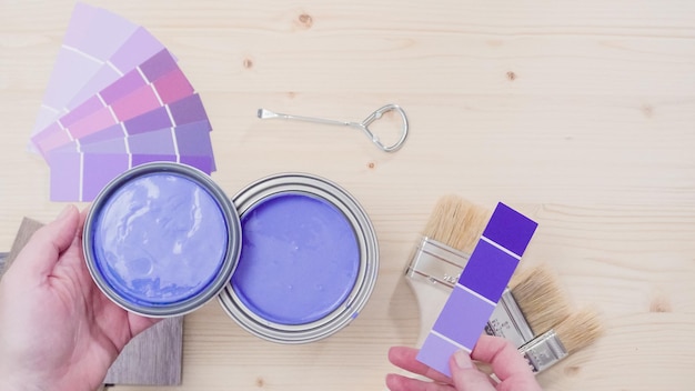 Boîte de peinture métallique ouverte avec de la peinture violette et d'autres outils de peinture sur fond de bois inachevé.