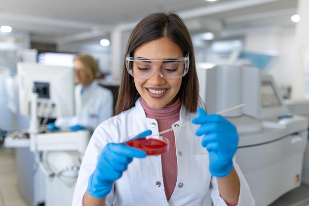 Boîte de Pétri à la main d'un jeune scientifique près d'un microscope en laboratoire Examen d'une plaque de culture bactérienne par une chercheuse en laboratoire de microbiologie