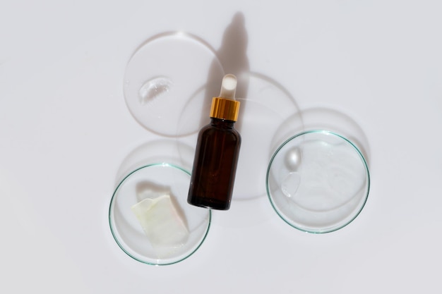 Photo boîte de petri en verre avec sérum pur transparent pour les soins de la peau avec sérum bouteille cosmétique sur fond blanc vue supérieure concept tests de laboratoire et recherche fabrication et test de cosmétiques