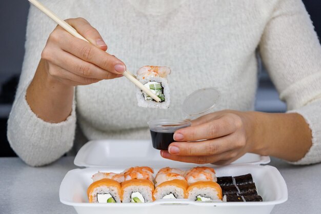 Une boîte de Philadelphie roule sur la table dans la cuisine Sushi de livraison rapide dans un récipient blanc La fille mange avec des baguettes Décoration festive Concept de Noël