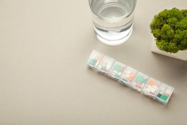 Boîte à pilules avec médicaments et verre d'eau sur fond gris Espace pour le texte